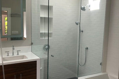 Inspiration for a medium sized modern ensuite bathroom in San Francisco with freestanding cabinets, dark wood cabinets, a freestanding bath, a double shower, a bidet, white tiles, ceramic tiles, grey walls, limestone flooring, an integrated sink, solid surface worktops, black floors, a hinged door and white worktops.