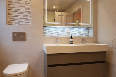 Large modern family bathroom in London with flat-panel cabinets, grey cabinets, a walk-in shower, a wall mounted toilet, beige tiles, porcelain tiles, beige walls, porcelain flooring, a wall-mounted sink, beige floors and an open shower.