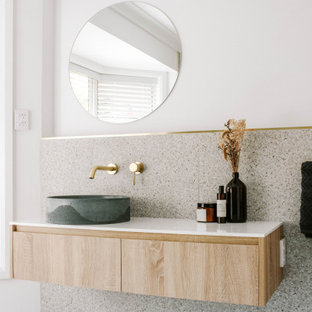 Idéer för industriella vitt en-suite badrum, med vita väggar, ett fristående handfat, granitbänkskiva, keramikplattor, terrazzogolv, släta luckor, skåp i ljust trä, grå kakel och grått golv