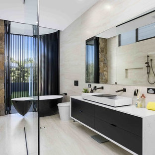 Photo of a contemporary master bathroom in Gold Coast - Tweed with flat-panel cabinets, black cabinets, a freestanding tub, an open shower, a one-piece toilet, beige tile, beige walls, a trough sink, concrete benchtops, beige floor, an open shower and grey benchtops.