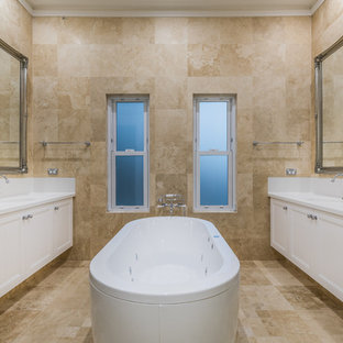 Design ideas for a victorian master bathroom in Perth with recessed-panel cabinets, white cabinets, a freestanding tub, beige tile, beige walls, an undermount sink, beige floor and white benchtops.