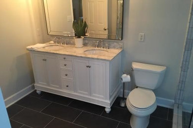 Example of a mid-sized minimalist master gray tile and ceramic tile ceramic tile and black floor corner shower design in Charlotte with furniture-like cabinets, white cabinets, a two-piece toilet, beige walls, an undermount sink, solid surface countertops, beige countertops and a hinged shower door
