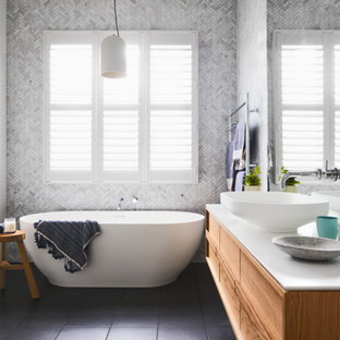 Photo of a transitional bathroom in Melbourne with flat-panel cabinets, medium wood cabinets, a freestanding tub, white walls, a vessel sink, grey floor and white benchtops.