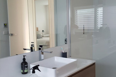 Modern inredning av ett mellanstort en-suite badrum, med släta luckor, vita skåp, en dusch i en alkov, vit kakel, porslinskakel, vita väggar, klinkergolv i porslin, ett integrerad handfat, granitbänkskiva, svart golv och dusch med gångjärnsdörr