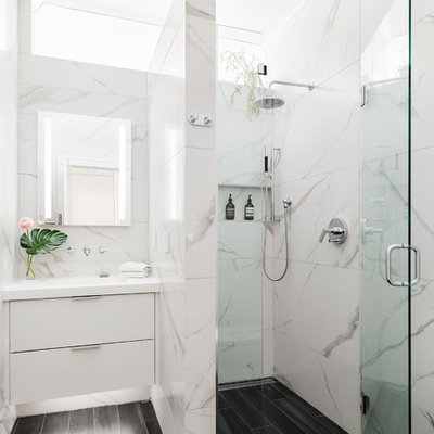 Example of a mid-sized trendy 3/4 porcelain tile and white tile porcelain tile and black floor walk-in shower design in Boston with flat-panel cabinets, white cabinets, white walls, an integrated sink, solid surface countertops, a hinged shower door and white countertops