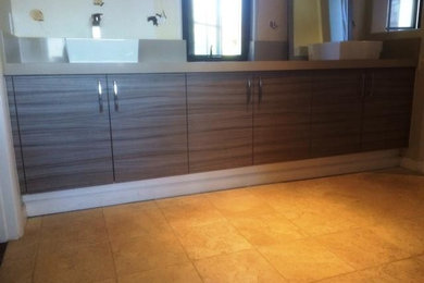 Cette photo montre une salle de bain principale chic en bois foncé de taille moyenne avec un placard à porte plane, un sol en travertin et une vasque.