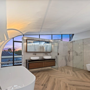 Inspiration for an expansive contemporary master bathroom in Sunshine Coast with a freestanding tub, a corner shower, a wall-mount toilet, white tile, porcelain tile, white walls, porcelain floors, a vessel sink, engineered quartz benchtops, beige floor, an open shower, black benchtops, a double vanity, a floating vanity, vaulted, flat-panel cabinets and medium wood cabinets.
