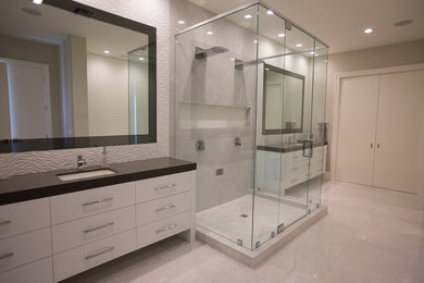 Corner shower - large modern master white tile and ceramic tile beige floor corner shower idea in Miami with flat-panel cabinets, white cabinets, white walls, an undermount sink, solid surface countertops, a hinged shower door and brown countertops