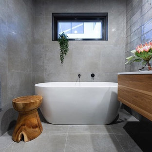 Inspiration for a mid-sized contemporary bathroom in Canberra - Queanbeyan with flat-panel cabinets, medium wood cabinets, a freestanding tub, gray tile, a vessel sink, grey floor and white benchtops.