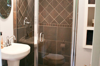ニューヨークにある高級な中くらいなコンテンポラリースタイルのおしゃれなバスルーム (浴槽なし) (ペデスタルシンク、レイズドパネル扉のキャビネット、白いキャビネット、アルコーブ型シャワー、一体型トイレ	、茶色いタイル、セラミックタイルの床、セラミックタイル、白い壁) の写真