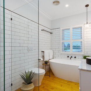 Photo of a contemporary bathroom in Melbourne with flat-panel cabinets, white cabinets, a freestanding tub, an open shower, a wall-mount toilet, white tile, white walls, light hardwood floors, a vessel sink, brown floor, an open shower and white benchtops.