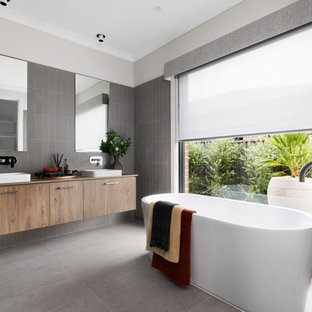 Photo of a contemporary master bathroom in Other with flat-panel cabinets, medium wood cabinets, a freestanding tub, gray tile, grey walls, a vessel sink, grey floor and brown benchtops.