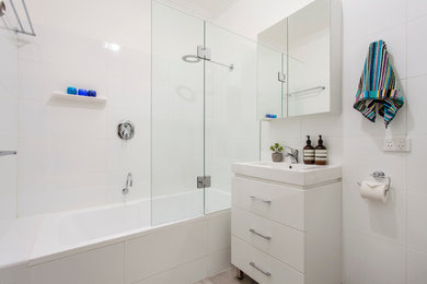 Ispirazione per una piccola stanza da bagno minimal con ante bianche, vasca da incasso, vasca/doccia, WC monopezzo, piastrelle bianche, pareti bianche e pavimento con piastrelle in ceramica