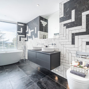 Large contemporary bathroom in Dorset with flat-panel cabinets, grey cabinets, a freestanding bath, a wall mounted toilet, black and white tiles, grey worktops, white walls, a vessel sink and black floors.