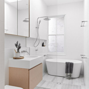 Photo of a mid-sized modern kids bathroom in Sydney with light wood cabinets, a freestanding tub, white tile, ceramic tile, white walls, porcelain floors, solid surface benchtops, grey floor, an open shower, white benchtops, a niche, a single vanity, a floating vanity, flat-panel cabinets, a curbless shower, a one-piece toilet and an integrated sink.