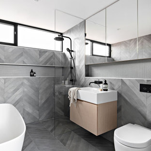 Design ideas for a mid-sized modern master bathroom in Sydney with light wood cabinets, a freestanding tub, gray tile, ceramic tile, grey walls, porcelain floors, solid surface benchtops, grey floor, an open shower, white benchtops, a niche, a single vanity, a floating vanity, flat-panel cabinets, a curbless shower, a one-piece toilet and an integrated sink.