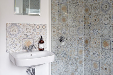 デヴォンにある中くらいなおしゃれな浴室 (オープン型シャワー、壁掛け式トイレ、マルチカラーのタイル、セラミックタイル、白い壁、塗装フローリング、壁付け型シンク、グレーの床、引戸のシャワー) の写真
