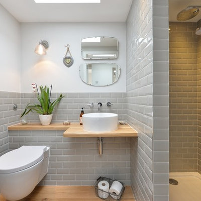 Example of a transitional gray tile and subway tile medium tone wood floor bathroom design in Other with a wall-mount toilet, white walls, a vessel sink, wood countertops and beige countertops
