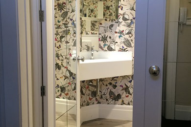 Immagine di una piccola stanza da bagno minimalista con ante di vetro, WC sospeso, pareti multicolore, pavimento in vinile, lavabo da incasso e top in superficie solida