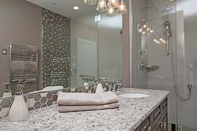 Example of a large classic master brown tile and porcelain tile porcelain tile and gray floor bathroom design in Other with raised-panel cabinets, gray cabinets, a two-piece toilet, gray walls, an undermount sink, quartz countertops and a hinged shower door