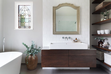 Exemple d'une grande salle de bain moderne en bois brun pour enfant avec un placard à porte plane, une baignoire indépendante, un espace douche bain, un carrelage blanc, des carreaux de céramique, un mur gris, un sol en carrelage de porcelaine, une grande vasque et un plan de toilette en verre.