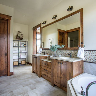 Diseño de cuarto de baño principal, rural, grande, con armarios estilo shaker, puertas de armario de madera oscura, bañera encastrada, paredes beige, suelo de piedra caliza y lavabo bajoencimera