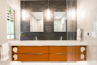This is an example of a large modern ensuite bathroom in Detroit with flat-panel cabinets, brown cabinets, a walk-in shower, a one-piece toilet, black tiles, stone tiles, beige walls, a submerged sink and solid surface worktops.