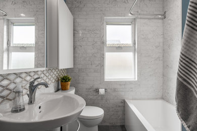 Cette image montre une petite salle de bain traditionnelle pour enfant avec une baignoire en alcôve, WC à poser, un carrelage blanc, des carreaux de porcelaine, un mur blanc, un sol en carrelage de porcelaine, un lavabo de ferme et un sol gris.