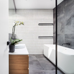 Photo of a contemporary master bathroom in Sydney with medium wood cabinets, a freestanding tub, a curbless shower, gray tile, a vessel sink, grey floor and white benchtops.
