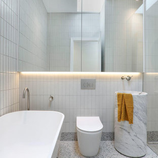 Modern bathroom in Melbourne with a freestanding tub, an alcove shower, a one-piece toilet, white tile, a pedestal sink and grey floor.