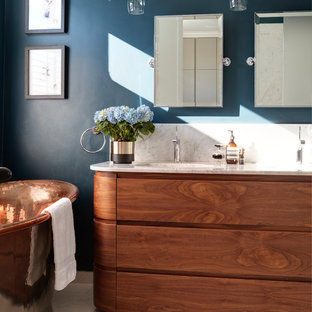Medium sized contemporary ensuite bathroom in London with a freestanding bath, blue walls, porcelain flooring, marble worktops, white worktops, freestanding cabinets, medium wood cabinets, a submerged sink and beige floors.