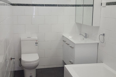 Cette photo montre une petite salle de bain moderne avec un placard à porte vitrée, des portes de placard blanches, une baignoire d'angle, un combiné douche/baignoire, WC suspendus, un carrelage blanc, des carreaux de porcelaine, un mur blanc, un sol en carrelage de porcelaine, un lavabo suspendu et un plan de toilette en stratifié.