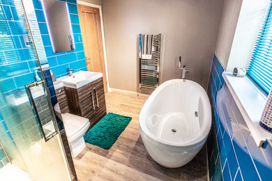 Photo of a modern ensuite bathroom in Cardiff with brown cabinets, a freestanding bath, a corner shower, a one-piece toilet, blue tiles, brown walls, brown floors and a hinged door.