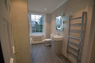 This is an example of a small contemporary ensuite bathroom in Other with a built-in bath, a shower/bath combination, a two-piece toilet, grey tiles, ceramic tiles, grey walls, cement flooring and a console sink.