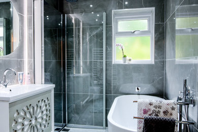 Photo of a medium sized contemporary ensuite wet room bathroom in Manchester with light wood cabinets, a freestanding bath, a wall mounted toilet, grey tiles, ceramic tiles, grey walls, porcelain flooring, a wall-mounted sink, grey floors and a hinged door.
