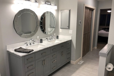Photo of a medium sized contemporary ensuite bathroom in Calgary with shaker cabinets, grey cabinets, marble worktops, a corner shower, white tiles, metro tiles, grey walls, porcelain flooring, a submerged sink, grey floors and a hinged door.