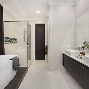 This is an example of an expansive contemporary master bathroom in Gold Coast - Tweed with engineered quartz benchtops, flat-panel cabinets, dark wood cabinets, a freestanding tub, a corner shower, beige tile, porcelain tile, porcelain floors, a vessel sink, beige floor, a hinged shower door and white benchtops.