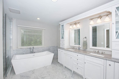 Large traditional ensuite bathroom in Cincinnati with raised-panel cabinets, white cabinets, a freestanding bath, a walk-in shower, a one-piece toilet, white tiles, marble tiles, grey walls, marble flooring, a submerged sink, granite worktops, grey floors and an open shower.