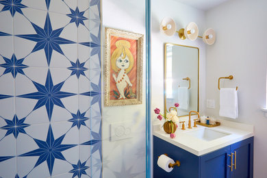 サンフランシスコにある高級な中くらいなビーチスタイルのおしゃれな浴室 (落し込みパネル扉のキャビネット、青いキャビネット、アルコーブ型シャワー、一体型トイレ	、青いタイル、白いタイル、セラミックタイル、白い壁、モザイクタイル、アンダーカウンター洗面器、クオーツストーンの洗面台、白い床、開き戸のシャワー、白い洗面カウンター) の写真