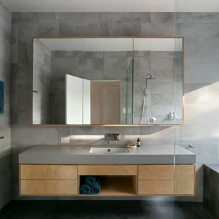 This is an example of a contemporary bathroom in Melbourne with flat-panel cabinets, medium wood cabinets, a drop-in tub, gray tile, grey walls, an undermount sink, black floor and grey benchtops.