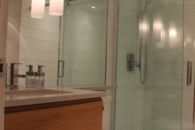 Modernes Badezimmer mit Unterbauwaschbecken, flächenbündigen Schrankfronten, hellen Holzschränken, Quarzwerkstein-Waschtisch, Duschnische, Toilette mit Aufsatzspülkasten, weißen Fliesen und Glasfliesen in Vancouver