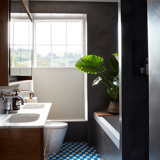 Inspiration for a medium sized contemporary bathroom in Devon with flat-panel cabinets, medium wood cabinets, a built-in bath, grey tiles, cement tiles, cement flooring, marble worktops, blue floors, an open shower, white worktops, black walls and a submerged sink.