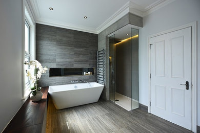 This is an example of a medium sized contemporary family bathroom in London with flat-panel cabinets, brown cabinets, a freestanding bath, a walk-in shower, a wall mounted toilet, grey tiles, ceramic tiles, white walls, ceramic flooring, a built-in sink, quartz worktops, grey floors, an open shower and white worktops.