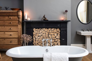 Design ideas for a large traditional ensuite bathroom in London with a pedestal sink, a claw-foot bath, grey walls, medium hardwood flooring and a chimney breast.