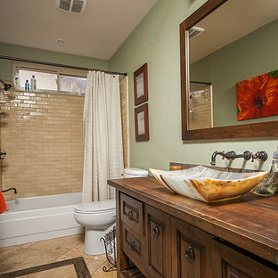 This is an example of a mid-sized transitional bathroom in Los Angeles with furniture-like cabinets, dark wood cabinets, an alcove tub, a shower/bathtub combo, a one-piece toilet, multi-coloured tile, stone tile, grey walls, travertine floors, a vessel sink and copper benchtops.