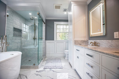 Bathroom - large transitional master white tile and marble tile porcelain tile, white floor, double-sink and wall paneling bathroom idea in New York with shaker cabinets, white cabinets, a one-piece toilet, gray walls, an undermount sink, marble countertops, white countertops and a freestanding vanity