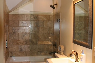ミルウォーキーにある高級な中くらいなトランジショナルスタイルのおしゃれなバスルーム (浴槽なし) (フラットパネル扉のキャビネット、黒いキャビネット、アルコーブ型浴槽、シャワー付き浴槽	、一体型トイレ	、茶色いタイル、石スラブタイル、ベージュの壁、スレートの床、一体型シンク) の写真