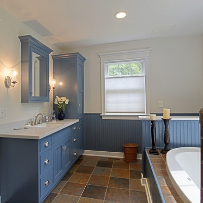 Example of a mid-sized arts and crafts slate floor drop-in bathtub design in Philadelphia with shaker cabinets, blue cabinets, white walls, an undermount sink and solid surface countertops