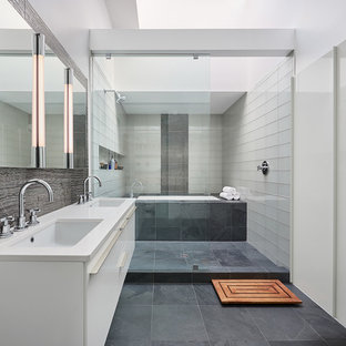 Example of a trendy master gray tile, white tile and glass tile porcelain tile bathroom design in DC Metro with flat-panel cabinets, white cabinets, white walls, an undermount sink, solid surface countertops and an undermount tub