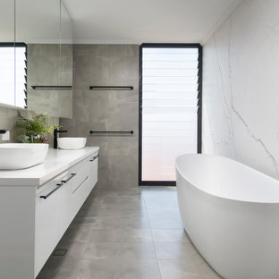 This is an example of a mid-sized contemporary master bathroom in Perth with flat-panel cabinets, white cabinets, a freestanding tub, gray tile, porcelain tile, pebble tile floors, a vessel sink, grey floor and white benchtops.